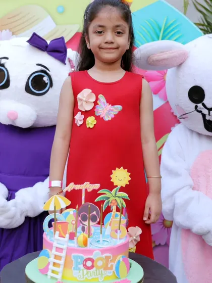 A birthday girl poses with our bunny mascots next to her pool party themed cake.
