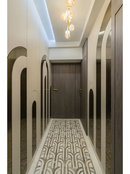 This passageway is designed to be a visual journey. It features arched wall motifs with bronze mirror inlays, a custom-designed floor inlay, and elegant pendant lighting that creates a warm and inviting path.