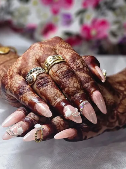Your nails are the final touch to your festive look. This beautiful Karwa Chauth set, featuring delicate 3D flowers and sparkling accents on long almond extensions, perfectly complements the intricate henna, creating a complete and elegant bridal style.