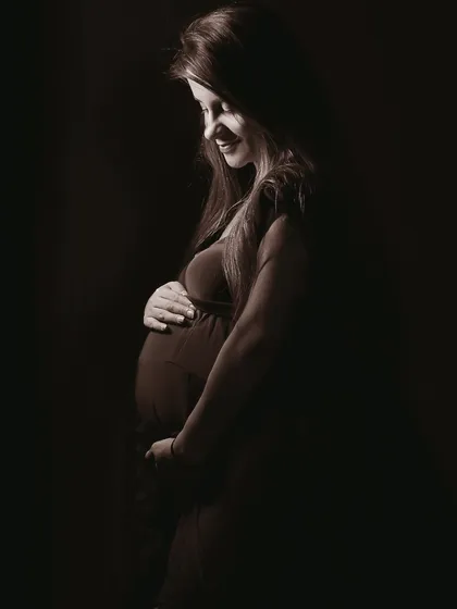 A quiet, artistic solo portrait using dramatic low-key lighting. This style creates a timeless and emotional image, focusing on the silhouette and the gentle light on the mother-to-be.