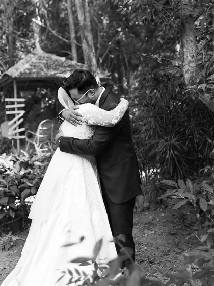 A wide shot of the couple embracing in a quiet garden setting. This photo provides context to their intimate first look, showing them sharing a private moment before the wedding ceremony begins.