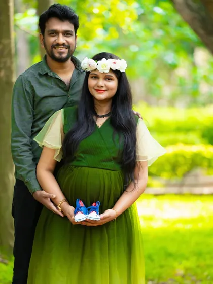 A lovely outdoor portrait announcing a baby boy. The couple holds up a tiny pair of blue baby shoes in a lush green park.