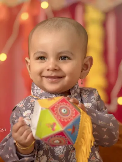 A close-up portrait from the Diwali session, focusing on the baby's bright smile as he holds a colorful lantern. The warm, glowing lights in the background create a beautiful bokeh effect.