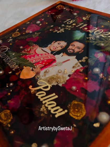 A closer look at the details that make a memory last. Here, you can see the preserved rose petals, delicate leaves, and pearl accents that surround the couple's photo in this custom varmala frame.