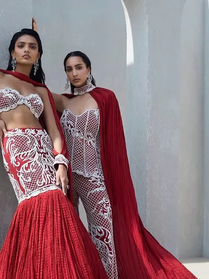 Crimson and pearl are a language of their own. I designed these two ensembles to be in conversation with each other. One, a sculpted fish-cut lehenga with a crushed drape, and the other, a fully embellished corset with embroidered pants and a sweeping cape, both speaking of contrast and cohesion.