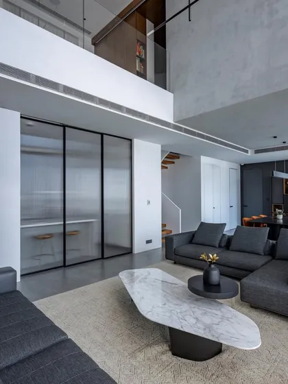 The living area of 'The Grey House', a duplex apartment in Mumbai. We embraced a minimalist aesthetic with a monochromatic grey palette, using textured walls and clean-lined furniture to create a space that is both sophisticated and calming. The double-height ceiling enhances the sense of openness and light.