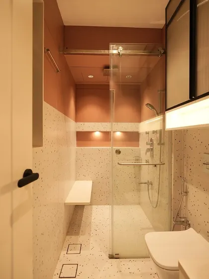 A full view of the modern bathroom, showing the glass shower partition, a built-in seating bench, and floor-to-ceiling terrazzo tiles for a cohesive and luxurious feel.