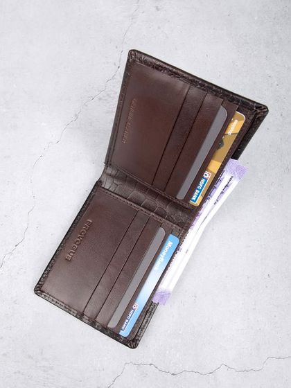 An open view of the dark brown crocodile wallet, filled with cards and cash to show its practicality.