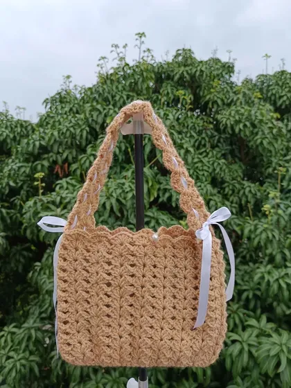 A beautiful shoulder bag in a lovely brown color, featuring a unique stitch pattern and delicate white ribbon details.
