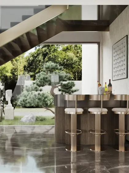 Detail is paramount in our luxury interiors. This close-up shows a custom-designed bar console with a gold-fluted metal finish, paired with elegant high stools. Positioned beneath a staircase, it offers a beautiful view of the garden, making it a perfect spot for entertaining.