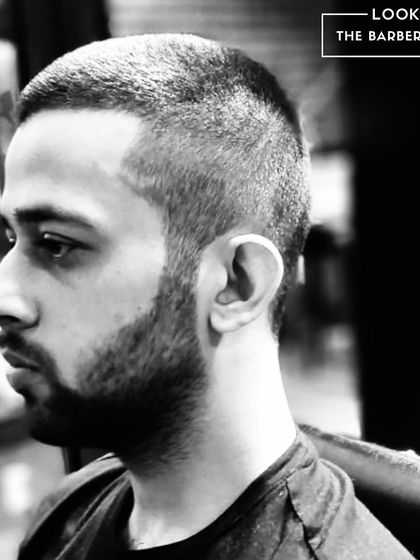 The buzz cut, executed with precision. This black and white shot highlights the clean lines of a fresh buzz cut and a defined beard shape for a strong, minimalist style.