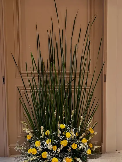 A close-up of the entrance arrangement, showing the texture of the tall green blades contrasted with the soft, bright yellow marigold flowers.
