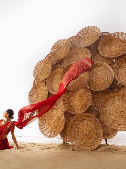 A moment of repose during a creative beach photoshoot. The flowing red fabric and the unique basket installation create a surreal and artistic composition.