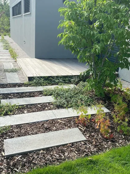 A contemporary pathway design using concrete pavers and bark mulch. This combination of materials is low-maintenance and provides a natural, textured look that complements the modern architecture.