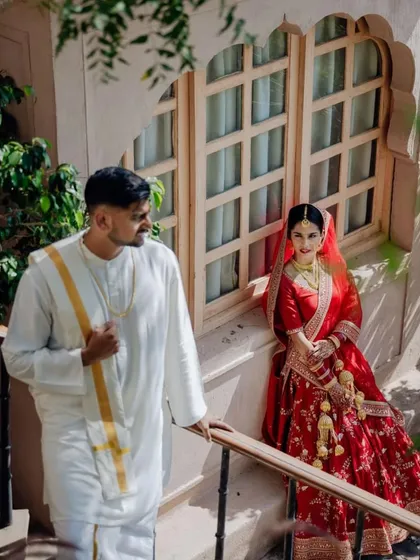 A quiet moment shared between the couple at their Rajasthan wedding. The simple white and red outfits stand out beautifully against the heritage architecture of the venue.