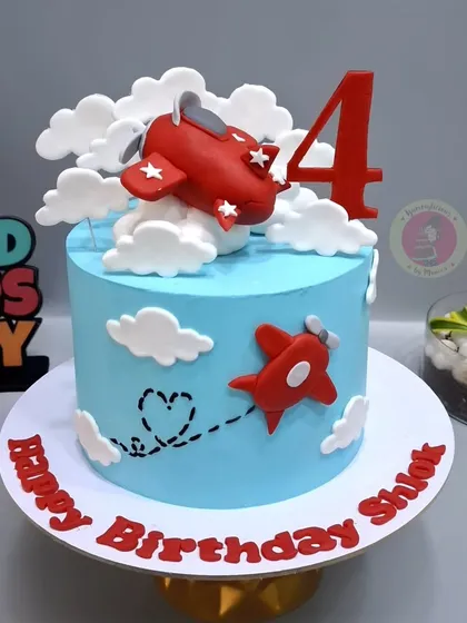 A simple and sweet airplane-themed cake, with a red plane flying through fluffy fondant clouds.