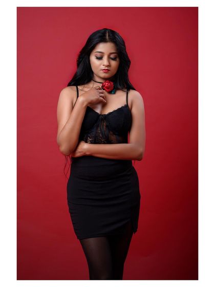 A full-length shot of a model in a black dress against a red background. The pose is strong and the color contrast is striking.