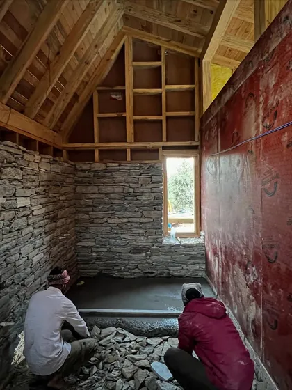 The interior of a guesthouse in Panchachuli during construction. The stone walls are laid by hand, and the floor is being prepared, showing the raw, elemental nature of the building process in this remote location.