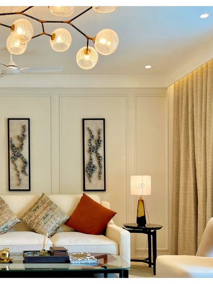 The living room of the DLF apartment is designed with a palette of soft neutrals, accented with pops of color in the cushions and artwork. A branching chandelier adds a modern, organic touch to the elegant space.