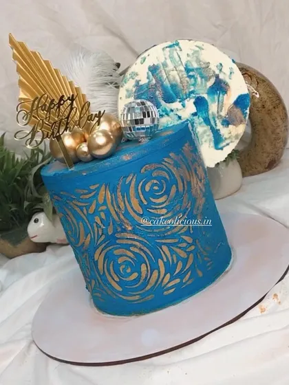 An asymmetrical cake I made for my brother's birthday. This modern design features a bold blue ganache with a gold stenciled pattern, topped with a disco ball, feathers, and an abstract chocolate sail.