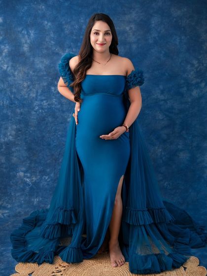 A powerful stance in a royal blue gown. This full-length portrait against a textured blue backdrop emphasizes the elegance of the dress and the confident posture of the mother-to-be.