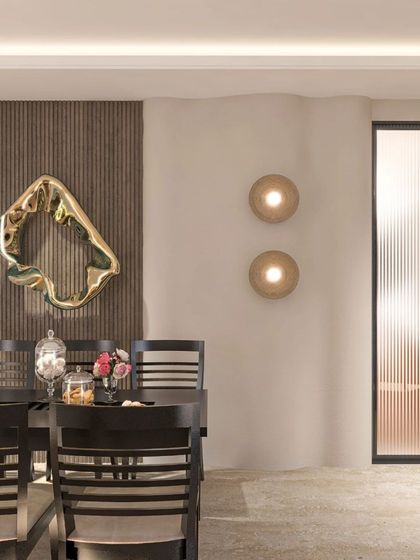A dining space that uses a striking gold-finished abstract wall sculpture as its focal point. The dark wood chairs and fluted glass partition add layers of texture and sophistication.