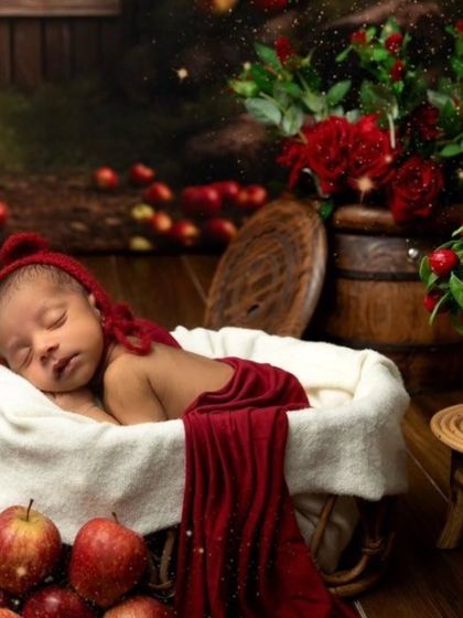 A beautiful portrait of a newborn sleeping in a basket, surrounded by the rich red colors of an apple-themed setup.