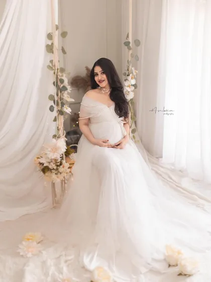 A full-length portrait of the mother-to-be on the swing, showcasing the beautiful flow of the white gown. The entire setup is designed to feel light, airy, and heavenly.