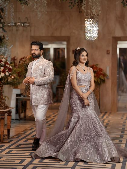 A full-length portrait of the couple in their stunning engagement attire. The bride's shimmering gown with a long train and the groom's embroidered jacket are showcased in this elegant, posed shot.