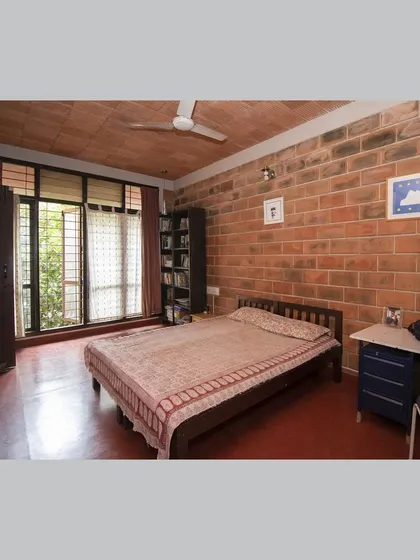 A bedroom with a filler slab ceiling, exposed brick wall, and a large window that opens to the outdoors.