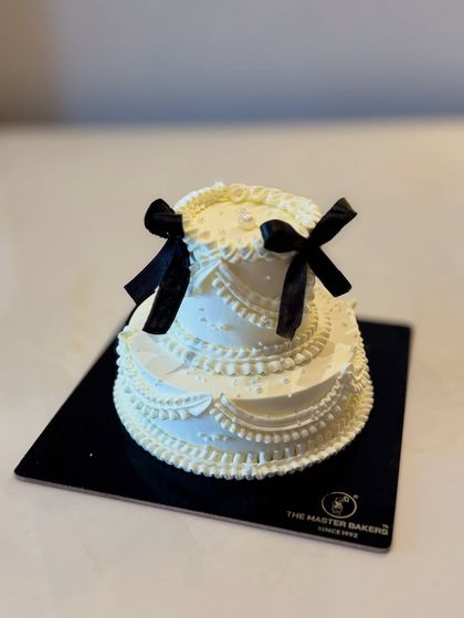 This striking two-tiered cake combines classic white piping with bold black ribbons for a timeless, monochromatic look. It's a sophisticated choice that makes a statement at any formal celebration.