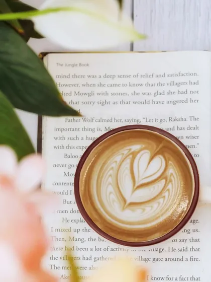 A perfect cup of latte with beautiful art rests on an open book. This classic pairing evokes a sense of quiet contemplation and the simple pleasure of a coffee break.
