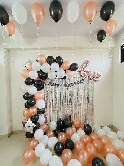 This birthday room decoration features a half-arch of black, white, and rose gold balloons against a silver fringe backdrop. I also added balloons floating on the ceiling to fill the room with a festive atmosphere.