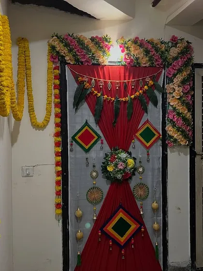 A simple door decoration for a home ceremony, using red drapes, floral corners, and traditional hangings.