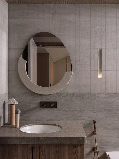 The guest bathroom continues the theme of artistic functionality. A custom-shaped mirror and a sleek, recessed light create a muted, sophisticated vibe.