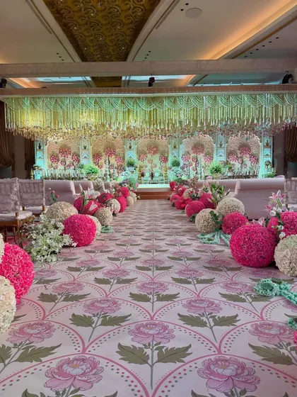 Every detail is an opportunity for artistry. This grand aisle, featuring a custom-printed lotus-motif carpet and lined with spheres of fresh pink and white roses, guides guests towards a ceremony steeped in beauty. 🌸