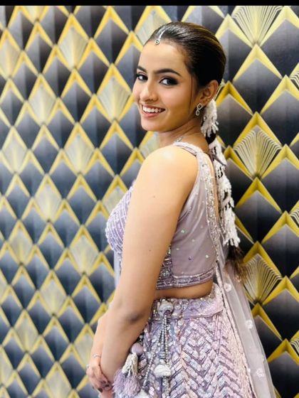 A smiling client posing against a stylish backdrop in the lavender lehenga.