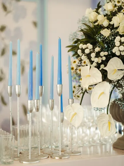 A close-up of tall, sky-blue taper candles in silver holders, adding a touch of modern elegance to the blue and white themed decor.
