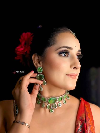 Elegance personified. This classic bun is adorned with a bright red flower, adding a pop of color that complements the stunning emerald jewelry and creates a sophisticated festive look.