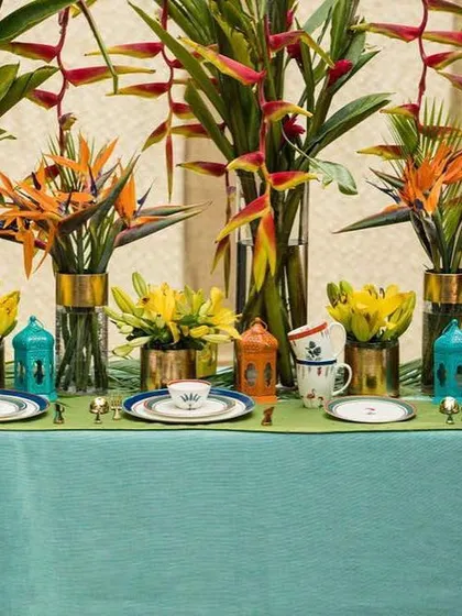 A close-up of the tablescape I styled for KIKA's tropical collection photoshoot. The arrangement features exotic flowers like Birds of Paradise and Heliconia in tall glass vases, set against a teal tablecloth to make the vibrant colors of the dinnerware pop.