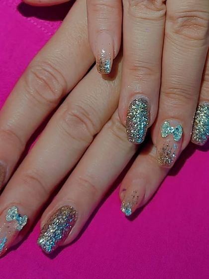 A fun and sparkly set of gel extensions with full-coverage silver and gold glitter, accented with cute 3D blue bows.