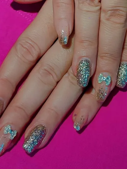 A fun and sparkly set of gel extensions with full-coverage silver and gold glitter, accented with cute 3D blue bows.
