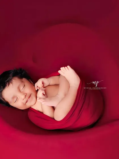 A heart-melting smile from a baby wrapped in a bold red swaddle. This minimalist setup puts all the focus on your newborn's expressions and tiny features, resulting in a timeless and striking portrait.