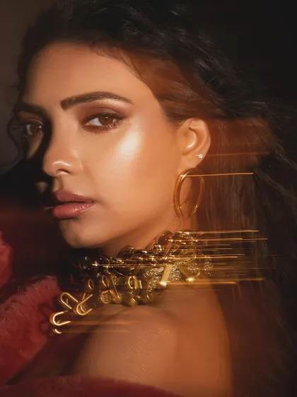 An artistic shot with a light trail effect, adding a dynamic and modern twist to a beauty portrait. The styling focuses on a statement gold necklace and glowing makeup.
