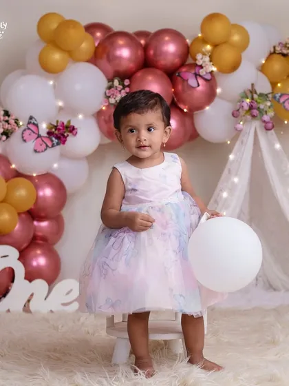 This pretty doll is standing tall for her first birthday portrait, surrounded by butterflies and balloons.