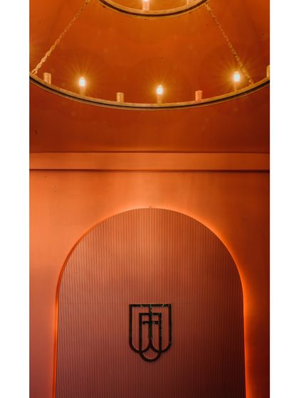 This image showcases the restaurant's branding integrated into the design. The logo is set against a textured, arched niche with warm backlighting, creating a memorable brand moment.