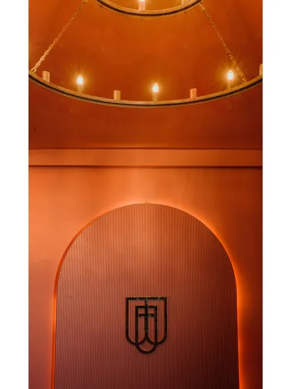 This image captures a branding moment within an arched niche, illuminated by a grand, circular chandelier. The warm, terracotta-colored walls and fluted texture create a rich and memorable brand statement.