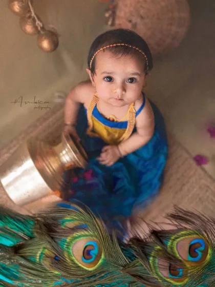 Introducing little Radha. This overhead shot captures her looking up, surrounded by peacock feathers, creating a beautiful and artistic composition.