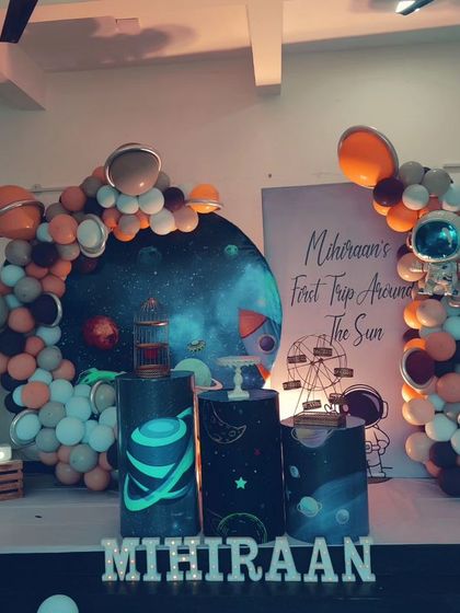 A "First Trip Around the Sun" space-themed birthday. This setup features a galaxy backdrop, astronaut cutouts, and a balloon arch with planet details.