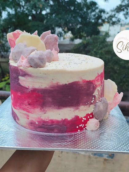 A simple yet beautiful cake with an abstract, textured finish in shades of pink and purple. The design is accented with shards of colored chocolate.